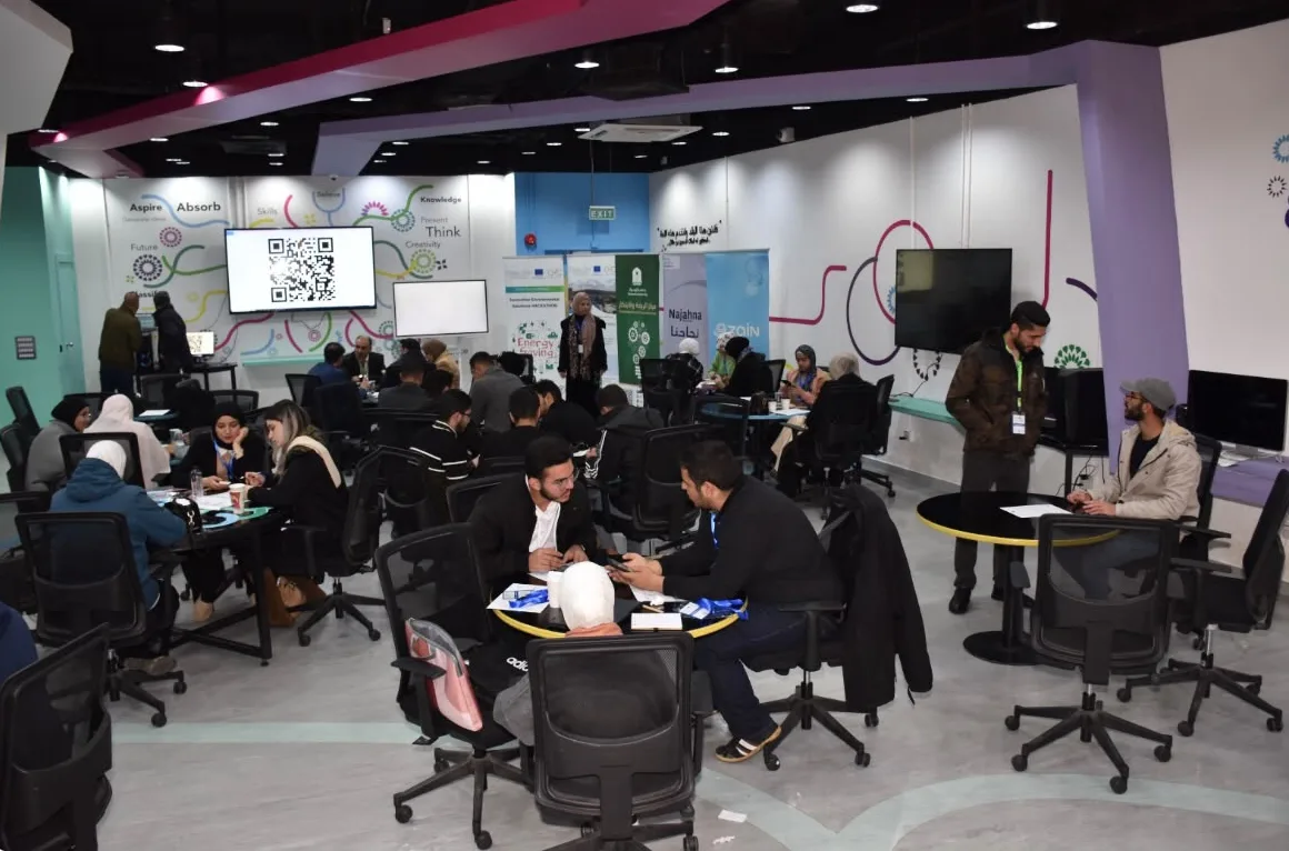 متدربون يعملون في مجموعات صغيرة حول طاولات مستديرة داخل قاعة ورش عمل حديثة.