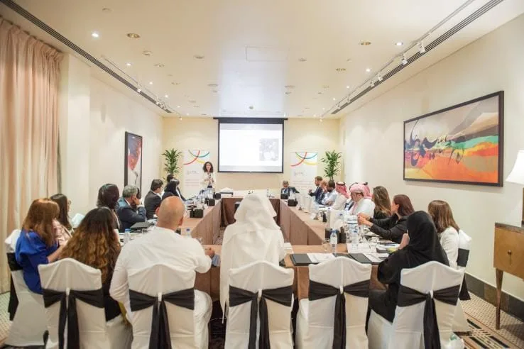ورشة عمل في قاعة اجتماعات: متدربون يجلسون حول طاولات مرتبة على شكل حرف U أمام شاشة عرض.