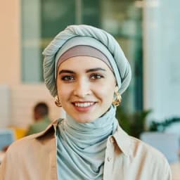صورة شخصية لامرأة مبتسمة ترتدي حجاباً، أمام خلفية مكتب مضيء.